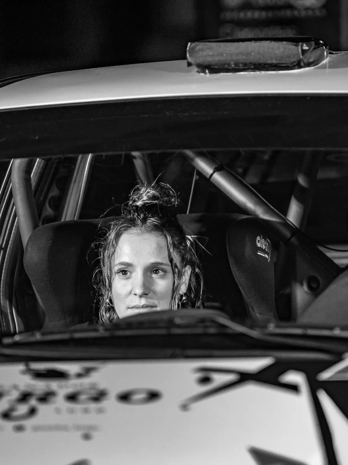 Laura Díaz, copiloto, dentro del coche de rally en parque cerrado nocturno, blanco y negro