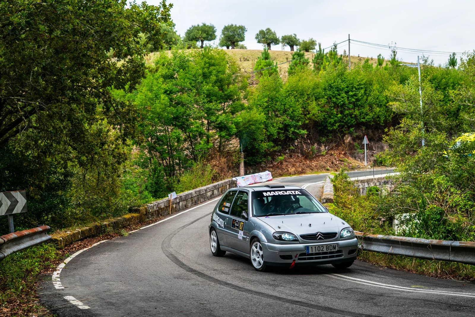 Citroën Saxo dorsal 87 con branding Margata en la Subida a Pontecaldelas 2025 sobre puente con vegetación gallega al fondo